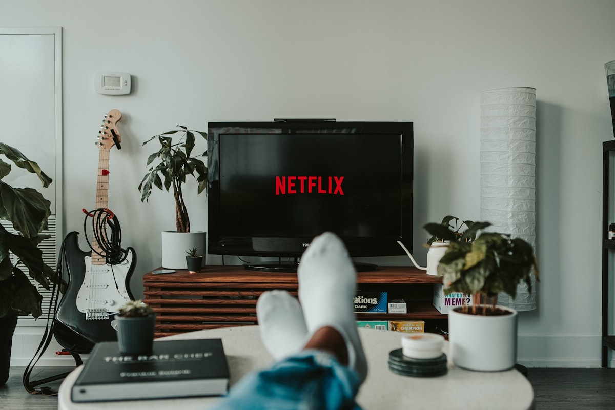 거실 소파에 앉아 TV 화면에 뜬 넷플릭스 가구 제한 메시지를 보며 당황해하는 남성의 뒷모습