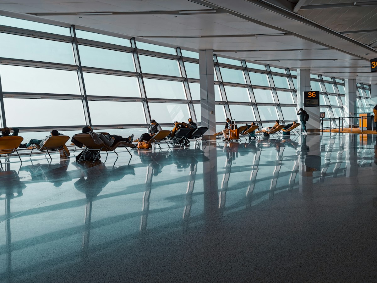 비행기 이륙 장면을 배경으로 공항 라운지 소파에서 태블릿을 보며 휴식을 취하는 여행자의 뒷모습