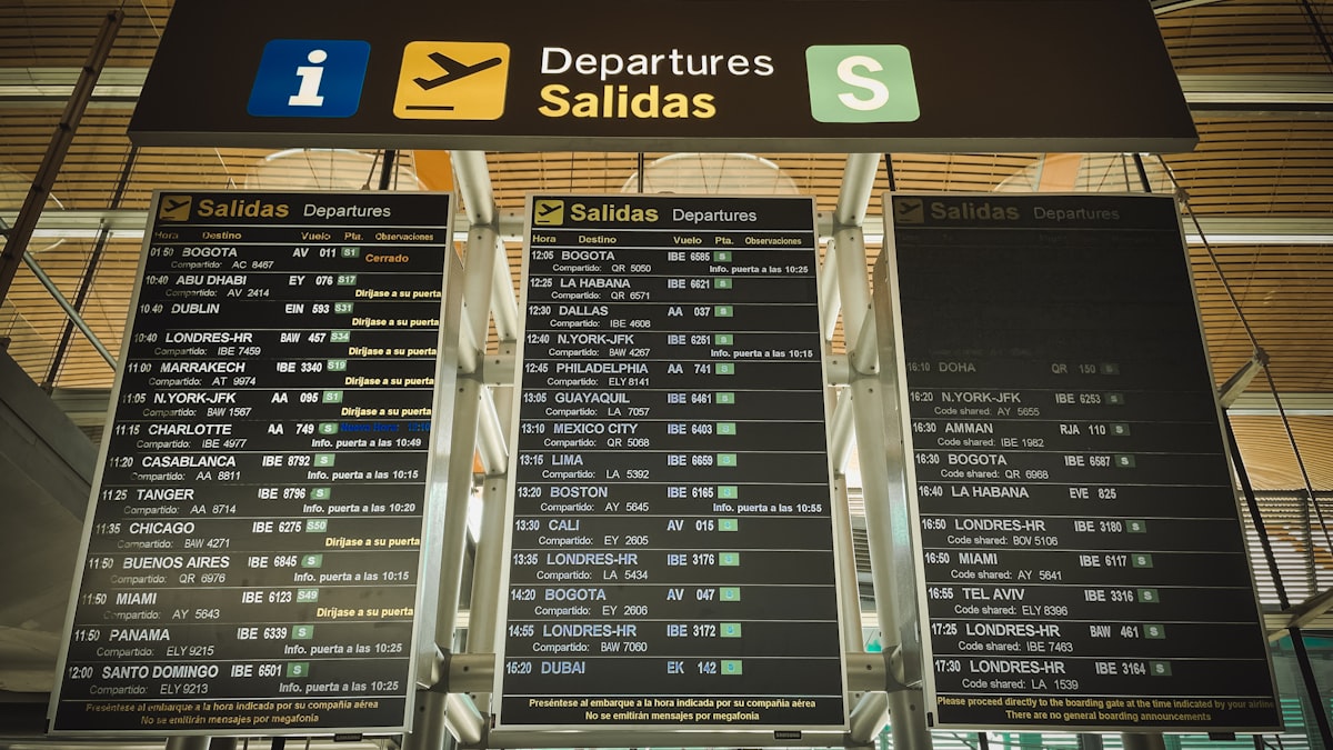 공항 터미널 전광판 앞에서 스마트폰 앱으로 항공권 가격을 긴박하게 확인하는 여행객의 뒷모습