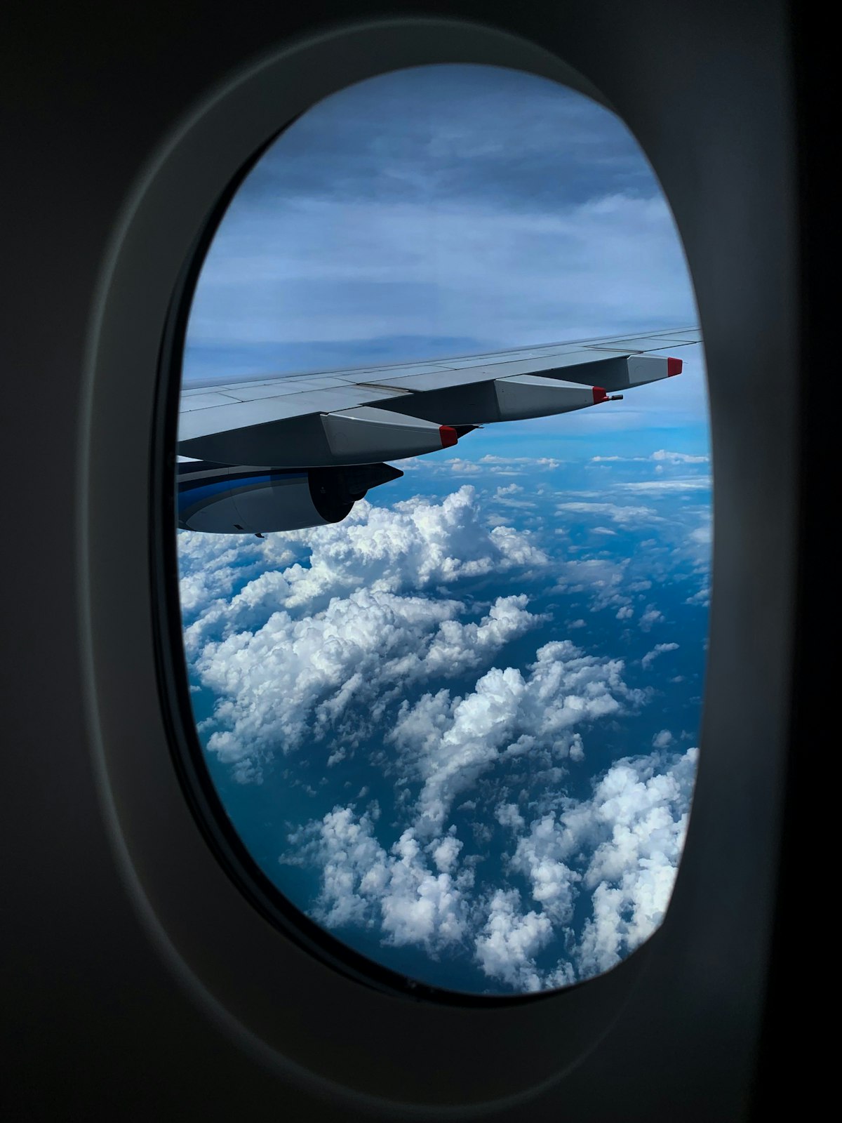 창밖으로 구름이 보이는 비행기 날개 옆 좌석에서 태블릿으로 저렴한 항공권을 검색하는 여행객의 모습